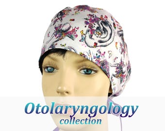 May include: A white scrub cap featuring a colorful pattern of anatomical ears, butterflies, and floral elements. The fabric is printed with detailed illustrations of ears in shades of gray, accented by vibrant pink, purple, and yellow flowers and butterflies.