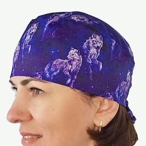 May include: A purple and blue scrub cap featuring a wolf and galaxy design. The cap is made of a soft fabric and is designed to cover the head and hair. The wolf design is in shades of purple and white.