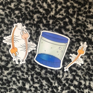 May include: Three stickers with cartoon illustrations. Two show a creature with a long, orange body, wings, and a smiling face. The third is a clear jar with a blue lid and base.