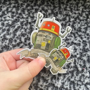 May include: Two stickers featuring a cartoon robot design with a red and yellow head, green accents, and a banner that reads "Certified Wax Content". The stickers are held by a hand.