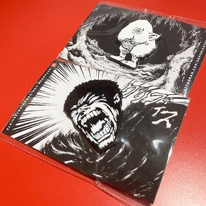 May include: Two black and white enamel pins. One pin features a screaming monster with sharp teeth. The other pin features a small, white, cartoon-like creature with a large head and a small body. The pins are on a white background with black and white illustrations.