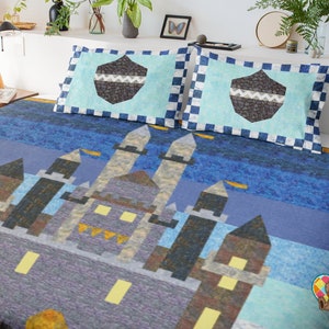 May include: A blue and grey quilt featuring a castle design. The quilt depicts a large castle with multiple towers and windows. The castle is set against a blue background with a subtle pattern. The quilt is made with a patchwork design and has a soft, comfortable feel.