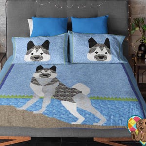 Peut inclure: Un ensemble de literie comprenant une couverture bleu clair et deux taies d'oreiller assorties. La couverture présente une illustration géométrique de chien debout sur un rocher brun près d'une eau bleue. Les taies arborent un motif de tête de chien.