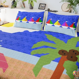Könnte beinhalten: Ein farbenfrohes Bettwäsche-Set mit einer Strandszene. Das Design umfasst einen blauen Ozean, einen Sandstrand, eine Palme und Segelboote mit bunten Segeln. Zwei Kissenbezüge mit Segelbootmustern sind zu sehen.