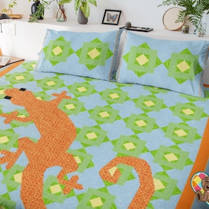 May include: A blue and green patterned quilt with a large orange gecko design. The quilt has a orange border and is made with a patchwork design.