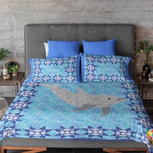 Puede incluir: Un edredón azul y blanco con un diseño de delfín. El edredón está en una cama con dos almohadas azules y una cabecera gris.