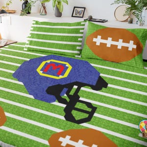 May include: A football-themed bedding set with a green field design and white lines. The set includes a pillowcase with a brown football design and another with green and white stripes. A blue helmet with a yellow and red letter is also featured.