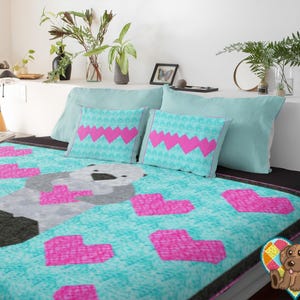 Peut inclure: Une courtepointe turquoise avec un motif de loutre grise et des cœurs roses. Deux coussins assortis avec des motifs de cœurs roses et un fond turquoise sont sur le lit. La parure de lit est sur un cadre de lit noir.