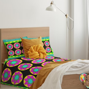 May include: A bed with a black, pink, green, and yellow patterned duvet cover and matching pillowcases. The bed has a yellow throw pillow with a knotted design. The bed is in a bedroom with white walls and a white lamp.