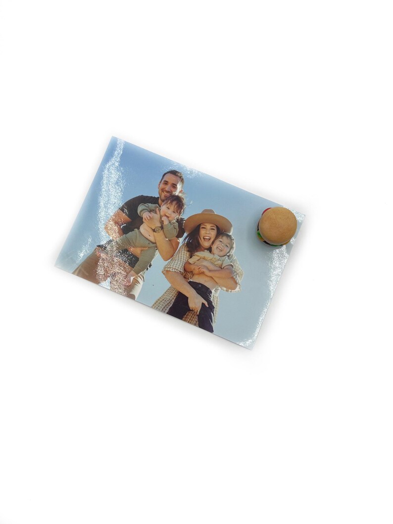 Peut inclure: Une planche &agrave; d&eacute;couper rectangulaire en verre avec une photo de famille et un accessoire de burger. La photo montre une famille de quatre personnes souriantes. Le burger a un pain, un steak, de la laitue et une tomate. Le fond est blanc.