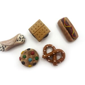 May include: A set of six miniature food-themed magnets, including a pretzel, a cookie with colorful sprinkles, a cannoli, a hot dog, and two graham cracker squares.
