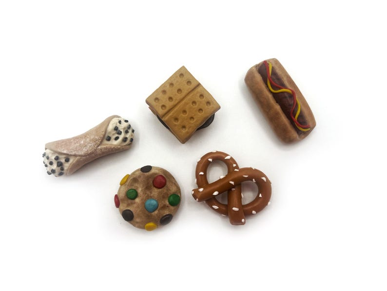 May include: A set of six miniature food-themed magnets, including a pretzel, a cookie with colorful sprinkles, a cannoli, a hot dog, and two graham cracker squares.
