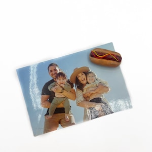 May include: A family photo of a couple holding their two children. The photo is printed on a glossy paper and has a hot dog magnet on top.