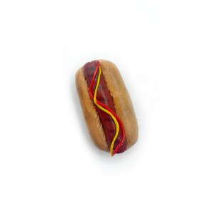 May include: A miniature hot dog with red ketchup and yellow mustard on a white background.