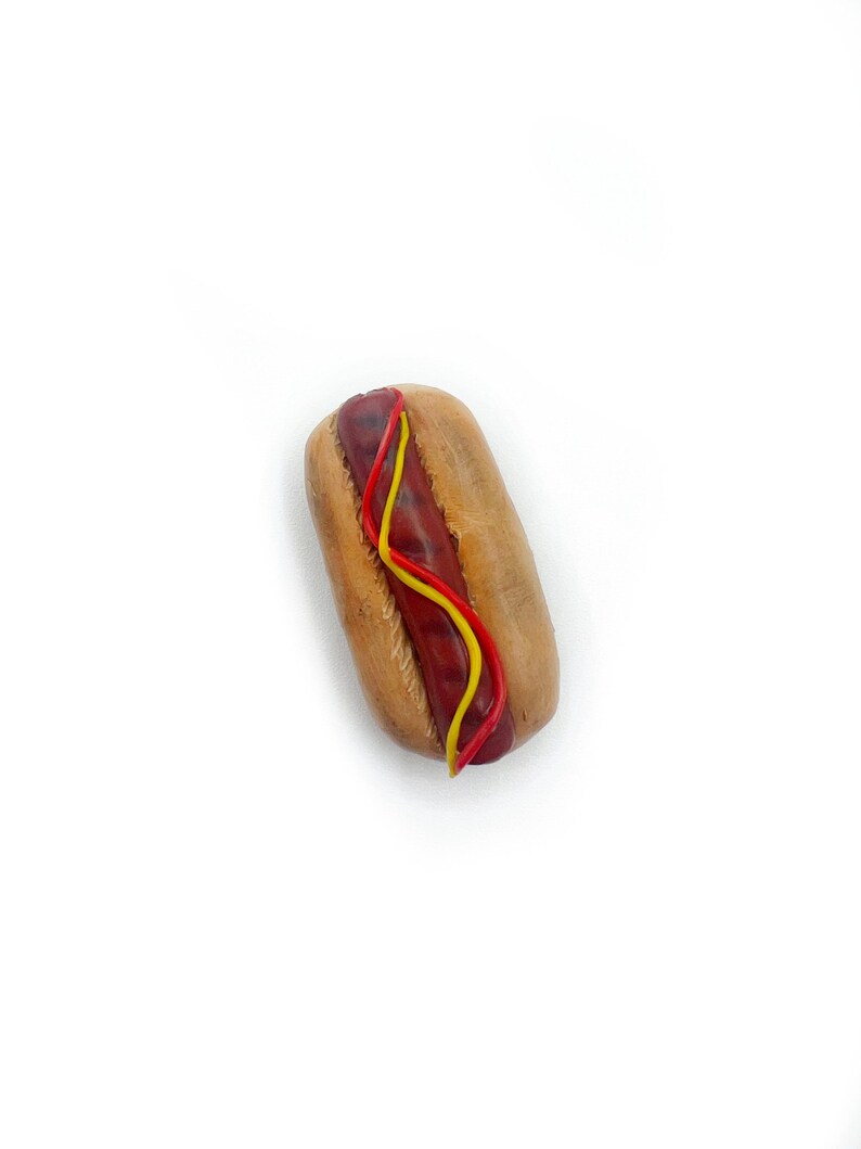 May include: A miniature hot dog with red ketchup and yellow mustard on a white background.