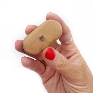 May include: A light brown oval-shaped object with a small silver magnet attached to the top.