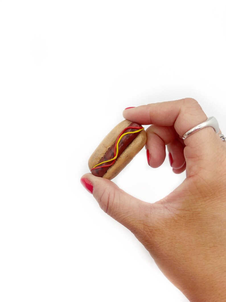 May include: A small wooden hot dog with red and yellow toppings.