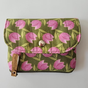 Peut inclure: Une petite pochette zippée matelassée verte avec un motif floral rose et une étiquette en cuir marron qui dit "Sambalulha".
