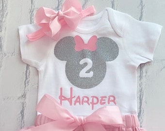 May include: A pink tutu with a white bodysuit featuring a silver glitter Minnie Mouse head with the number 2 and the name "Harper" in a Disney font.
