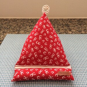 May include: Red triangular pillow with a white horseshoe pattern and a white and red striped band. The pillow has a loop handle and a brown leather tag that says "Hand Made".