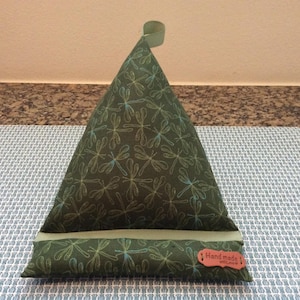 May include: A green and blue fabric phone stand with a dragonfly pattern. The stand has a light green fabric strip across the middle and a brown leather tag that says "Handmade with love".