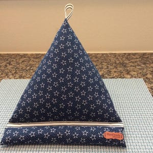 May include: A navy blue triangular book holder with white star patterns. It has a white stripe at the base and a small brown tag that says "Handmade". A striped loop is at the top.