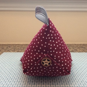 May include: A burgundy fabric doorstop with white stars and a wooden star button. The doorstop is shaped like a pyramid with a loop handle.