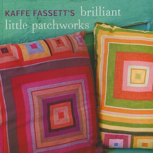 以下が含まれることがあります： 幾何学模様のカラフルなパッチワークのクッションが2つ。クッションは緑色の表面の上に置かれています。画像の上部には「Kaffee Fassett's brilliant little patchworks」というテキストがあります。画像の下部には「20 stitched and patched projects using Kaffe Fassett fabrics」というテキストがあります。