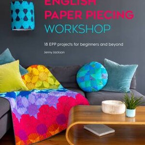 May include: A book titled "English Paper Piecing Workshop" with a colorful quilt on a couch and a wooden coffee table. The book cover features the title in pink and white text and the subtitle "18 EPP projects for beginners and beyond" in black text. The author, Jenny Jackson, is listed below the subtitle.