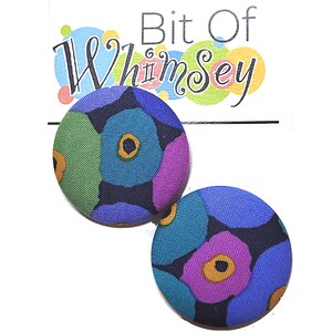 May include: A pair of round button earrings with a colorful floral pattern. The earrings feature a design of blue, green, purple, and yellow flowers on a dark blue background. The text "Bit Of Whimsy" is visible in the background.