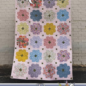 May include: A handmade quilt with a light pink background and large floral patterns in various colors. The quilt features the name "Maureen" in script and the Running Doe Quilts logo.