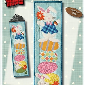 May include: A digital embroidery pattern for an Easter egg hunt wall hanging. The pattern features a bunny rabbit holding a carrot and a flower, standing on top of a stack of colorful eggs. The pattern is 6 inches wide by 22 inches long. The pattern is labeled "Easter Egg Hunt" and "Skill Level: EASY".