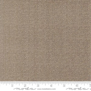 May include: A tan fabric featuring a repeating pattern of small, dark brown circles arranged in a grid. A white ruler is visible at the bottom, showing measurements in inches. The text "moda" and "www.modafabrics.com" is printed on the ruler.