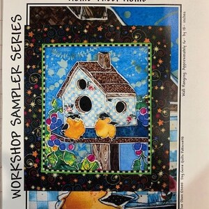 May include: A colorful quilt pattern featuring a birdhouse with two birds perched on a branch. The birdhouse is painted blue and white with a checkered pattern. The birds are yellow with black accents. The background is a blue sky with white clouds. The quilt pattern is titled "Home Tweet Home" and is part of the "Workshop Sampler Series".