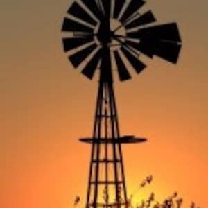 Pode incluir: Silhueta de um moinho de vento preto contra um pôr do sol laranja vibrante. O moinho de vento tem um design tradicional com uma torre alta e um grande ventilador de múltiplas pás.