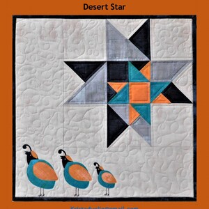 Könnte beinhalten: Ein Quiltblock mit einem Sternmuster in Grautönen, Schwarz, Türkis und Orange. Der Block ist von einem weißen Hintergrund mit einem gesteppten Muster umgeben. Drei kleine gestickte Wachteln befinden sich am unteren Rand des Blocks. Der Text "Trouble & Boo Designs" und "Desert Star" befindet sich über dem Block.