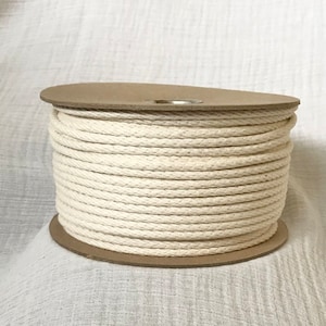 May include: A spool of natural white cotton rope. The rope is wound tightly around a cardboard spool.