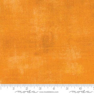 Może przedstawiać: Jednolity pomarańczowy materiał z subtelnym, fakturowanym wzorem. Materiał jest jednokolorowy z niewielką różnicą w odcieniu pomarańczowego. Materiał jest pokazany z linijką, na której widnieje napis "moda" i "www.modafabrics.com".