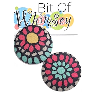 May include: Two round fabric buttons with a black background and a colorful floral pattern. The pattern features pink, yellow, and teal colors.