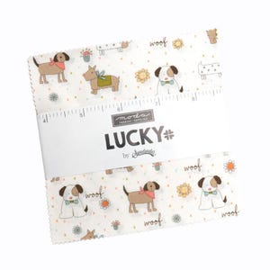 May include: A stack of fabric squares with a repeating pattern of cartoon dogs, flowers, and the word "woof" on a white background. The fabric is labeled "LUCKY" by Sweetwater. A ruler is printed on the fabric.