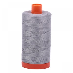 Puede incluir: Una bobina de hilo de coser gris con una bobina de plástico naranja.