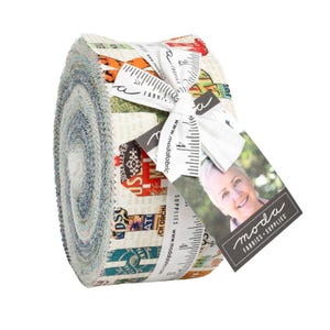 Könnte beinhalten: Ein gerolltes Bündel aus Stoffstreifen mit einer Vielzahl von bunten Mustern und Designs. Der Stoff ist mit einem weißen Band gebunden, das mit Messmarkierungen und dem Text "FABRICS + SUPPLIES" bedruckt ist. Ein Etikett mit dem Logo "moda FABRICS + SUPPLIES" ist angebracht.