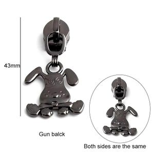 May include: A black metal zipper pull shaped like a cartoon dog. The dog is sitting on its hind legs with its front paws outstretched. The zipper pull is 43 mm tall. Gun balck. Both sides are the same.