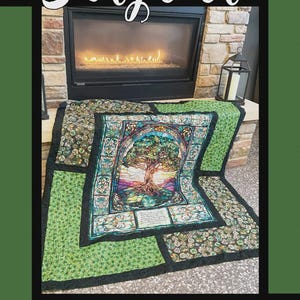 May include: A colorful quilt with a tree of life design, displayed in front of a fireplace. The quilt features a stained-glass effect with shades of green, blue, and purple. The word "Storyteller" is at the top. The quilt is by Tricia Lynn Maloney.