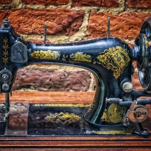 May include: A vintage black sewing machine with gold accents and a wooden base. The machine has a large wheel on the right side and a needle in the front.