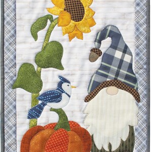 Könnte beinhalten: Ein Patchwork-Quiltblock mit einem Gnom mit einem blau-weiß karierten Hut, einem Blauhäher, der auf einem Kürbis sitzt, und einer gelben Sonnenblume.