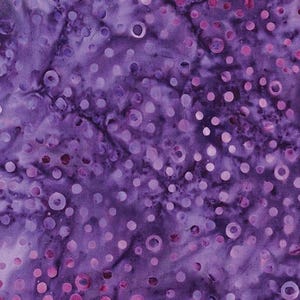 Op de afbeelding: Een close-up van een stof met een batikontwerp. De stof heeft een dieppaarse achtergrond met een patroon van cirkels van verschillende grootte in tinten paars en roze. De cirkels hebben een lichtere, bijna witte kern.