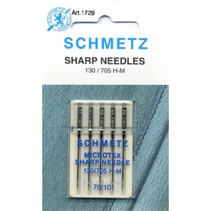 Puede incluir: Un paquete de cinco agujas de coser plateadas etiquetadas "Schmetz Microtex Sharp Needle 130/705 H-M 70/10".
