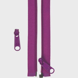 May include: A close-up of a purple zipper with a matching pull tab. The zipper is open, revealing the teeth and the fabric tape. The pull tab is a solid purple color with a hole for easy gripping. The background is a solid white.