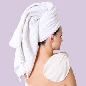 Puede incluir: Una mujer con una toalla blanca envuelta alrededor de su cabeza está usando un guante exfoliante blanco en su espalda.